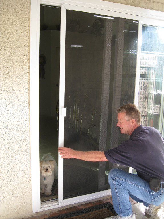 ALL-WAYS SCREENS technician demonstrating a sliding screen door with a dog inside